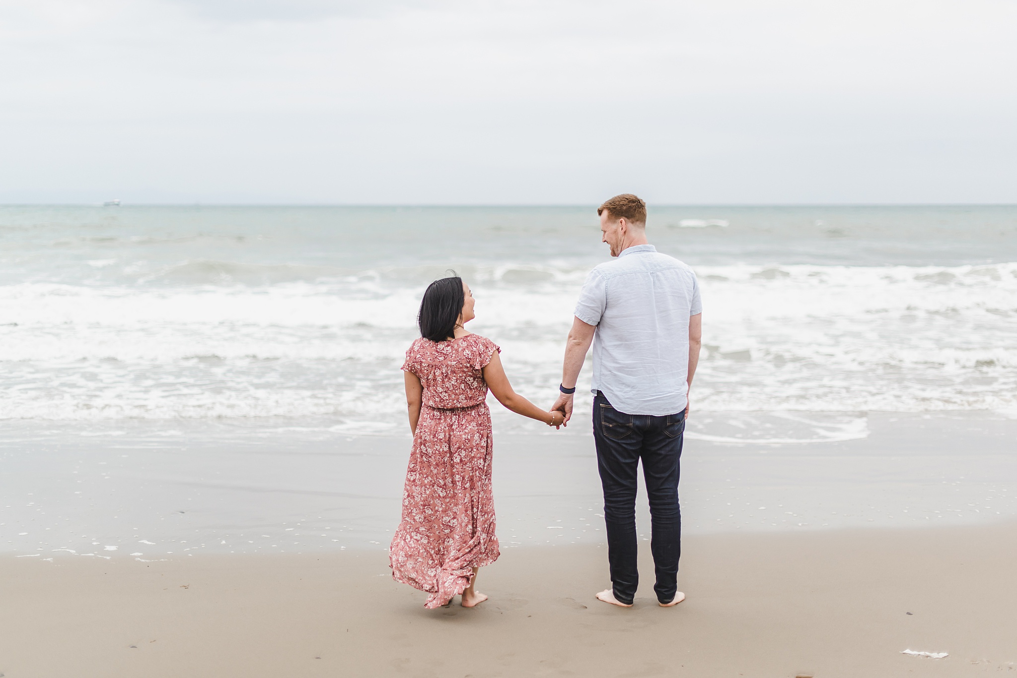 couple holding hands and facing the ocean